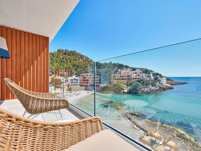 Balkon met rieten stoelen en glazen balustrade met uitzicht op zee en huizen aan de kust.