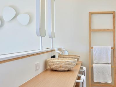 Lichte badkamer met houten accenten, witte wanddecoratie en gevlochten wasbak