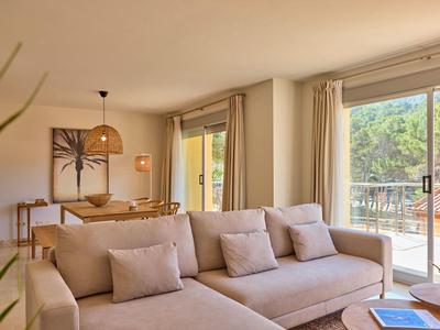 Lichte woonkamer met beige bank, eettafel en balkon met uitzicht op groen.