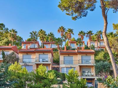 Varias casas de vacaciones modernas con balcones y palmeras bajo un cielo soleado.