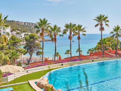 Área de piscina al aire libre con palmeras y vista al mar bajo un cielo azul.