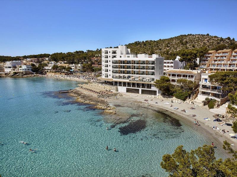 Kustzicht met helder water, strand, hotels en beboste heuvels op de achtergrond.
