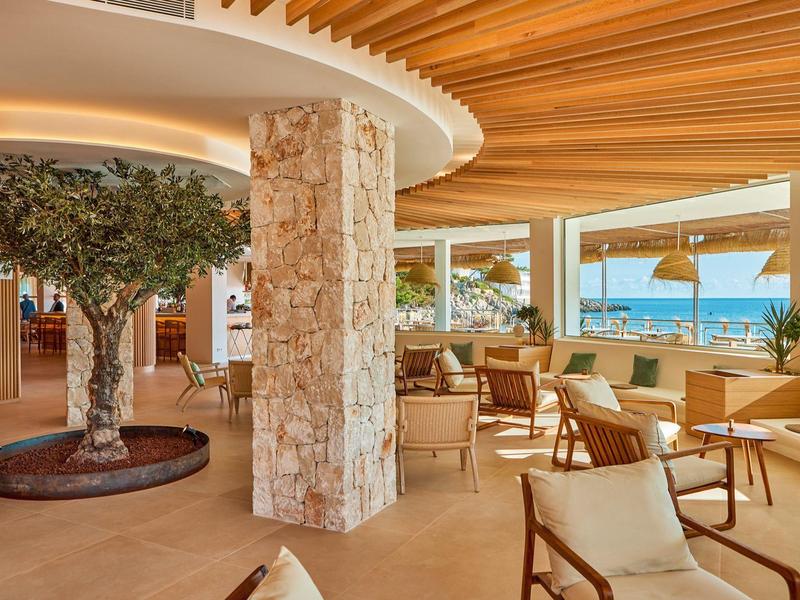 Lichte hotel/lounge met houten plafond, stenen zuilen en uitzicht op zee.