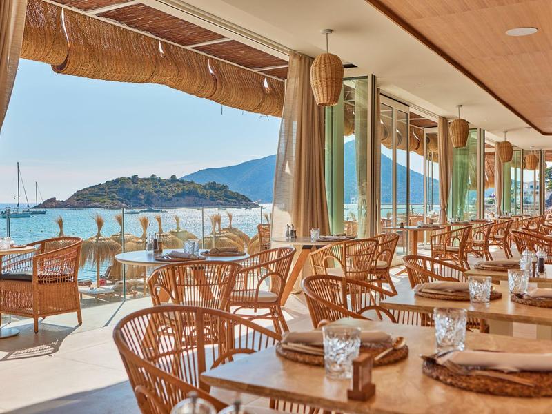 Open strandterras met houten tafels, stoelen en uitzicht op de zee en een eiland.