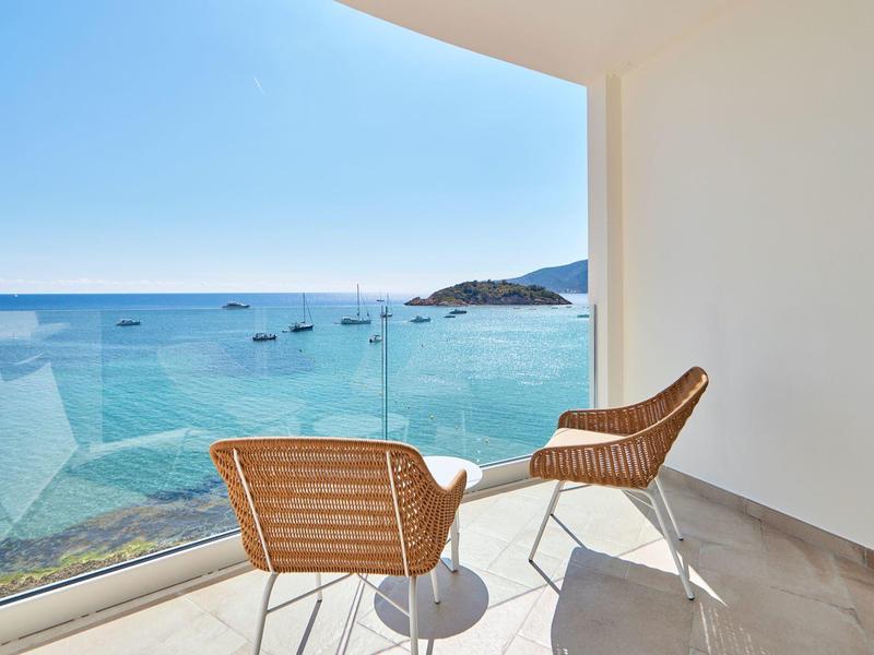 Balkon met twee stoelen en een tafel met uitzicht op zee en boten.