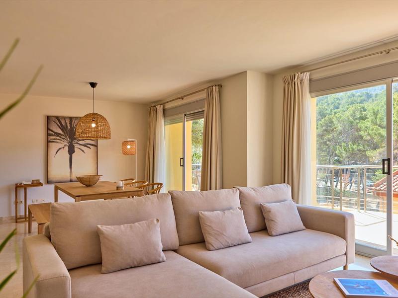 Lichte woonkamer met beige bank, eettafel en balkon met uitzicht op groen.