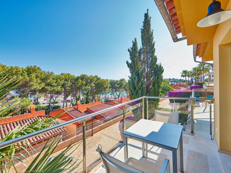 Balkon met tafel en stoelen met uitzicht op bomen en rode daken onder een blauwe lucht.