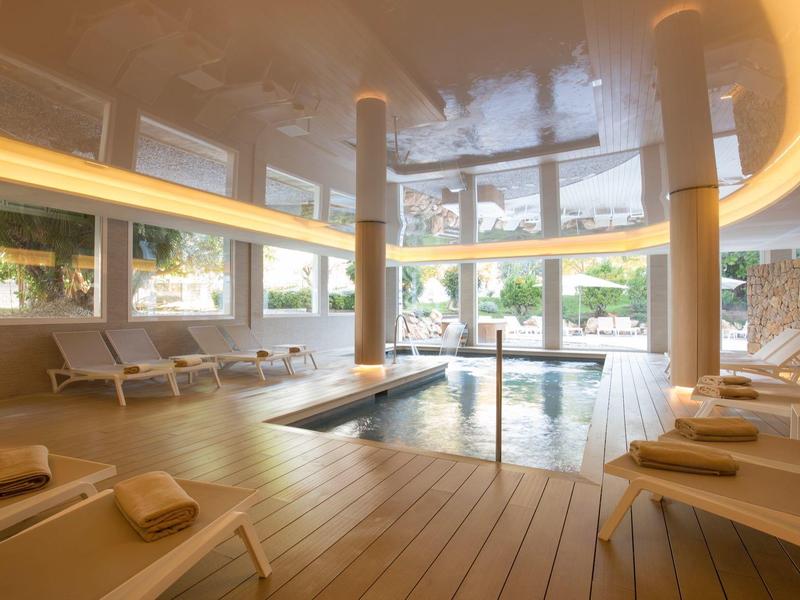 Innenraum eines hellen Wellnesspools mit Liegestühlen, Holzfußboden und großen Fenstern.