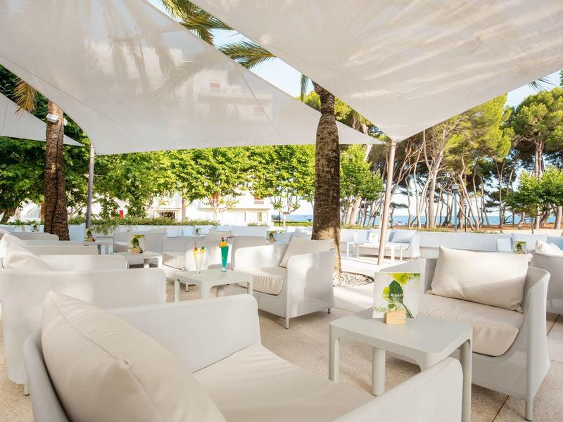 Helle, luftige Lounge mit weißen Sofas, kleinen Tischen und Sonnensegeln im Freien.