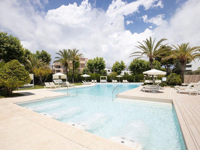 Großer Pool mit klarem Wasser, umgeben von Liegestühlen, Palmen und blauen Himmel mit Wolken.