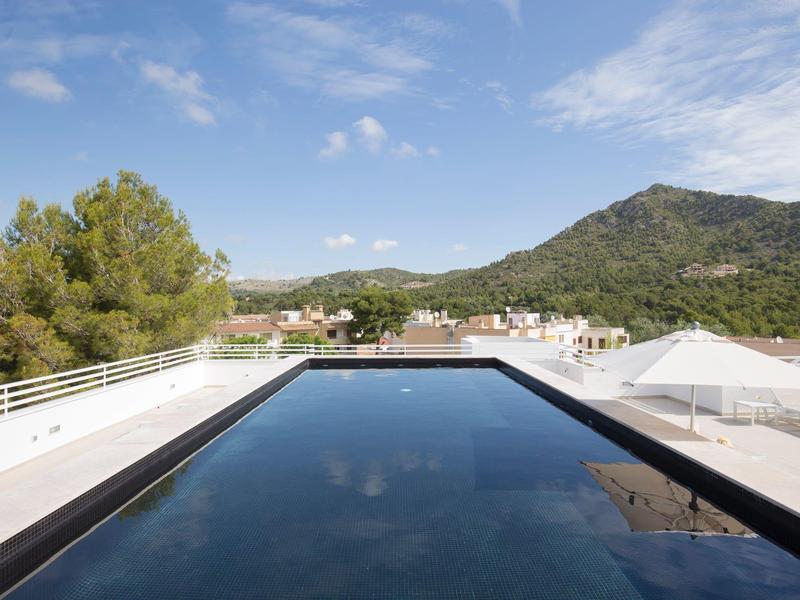 Moderner Dachpool mit klarer Wasseroberfläche, umgeben von Sonnenliegen und grünen Hügeln im Hintergrund.