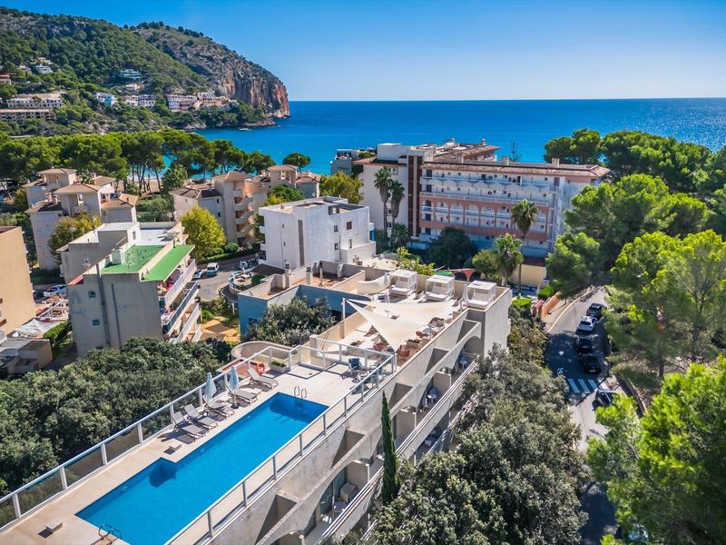 Blick auf eine Küstenstadt mit Pool auf dem Dach, grünen Bäumen, Gebäuden und blauem Meer im Hintergrund.