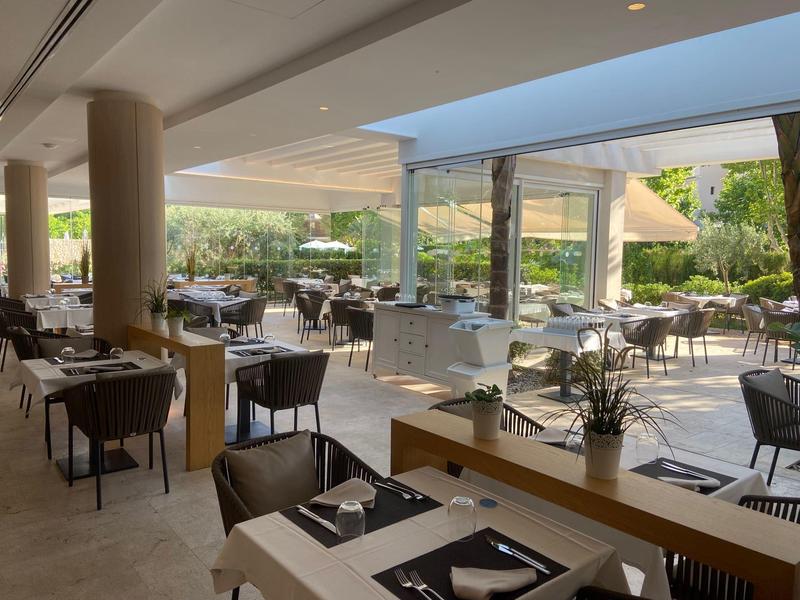 Modernes Restaurant mit vielen Tischen und Stühlen, großer Glasfront und heller, offener Atmosphäre.