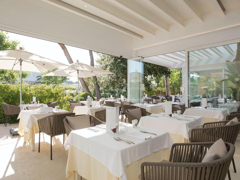 Moderner Außenbereich eines Restaurants mit weißen Tischen, Stühlen und großen Sonnenschirmen.