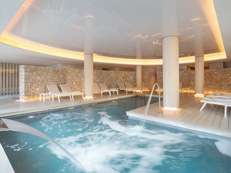 Innenpool mit Whirlpool, weißen Liegestühlen und moderner Beleuchtung an der Decke.