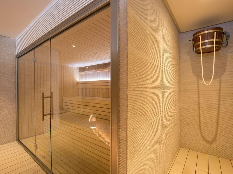 Moderne Sauna mit Glaswand, Holzbänken und hölzernem Saunaeimer an der Wand.