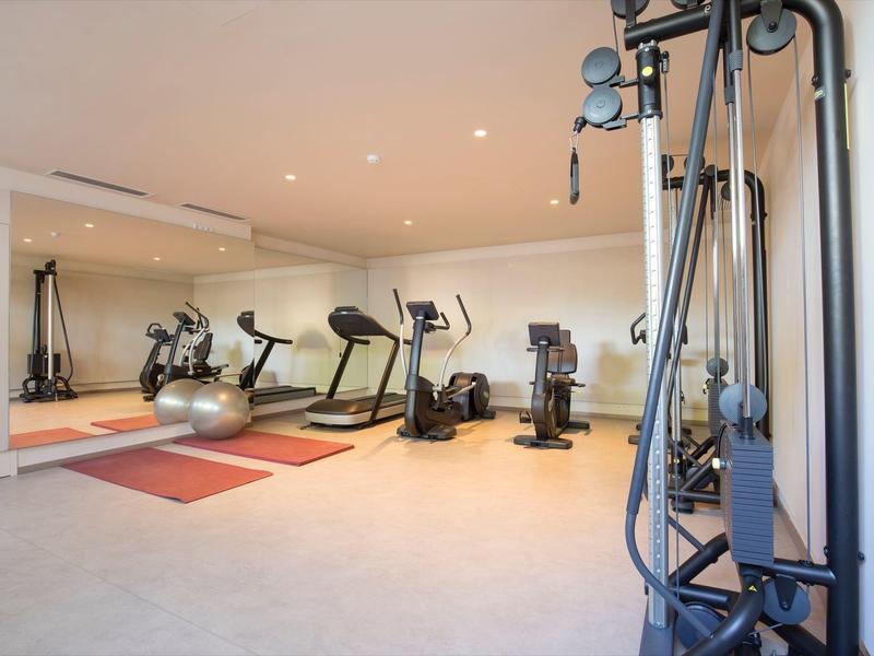 Heller Fitnessraum mit verschiedenen Sportgeräten und großem Wandspiegel.