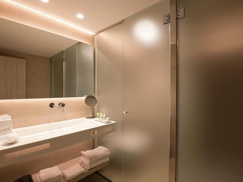 Modernes Bad mit großem Spiegel, Waschtisch, Handtüchern und schattierter Glastür.