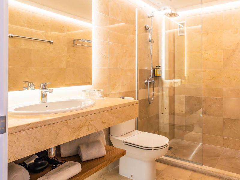 Helles Badezimmer mit beigem Marmor, großer Spiegel, Waschbecken, WC und Glas-Dusche.