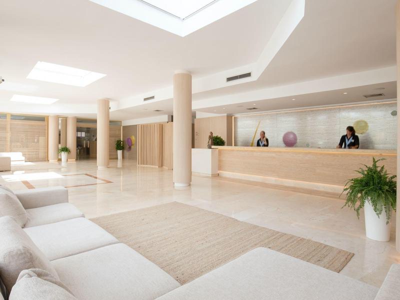 Heller, moderner Empfangsbereich mit Sofa, Holztheke und großer Fensterfront.