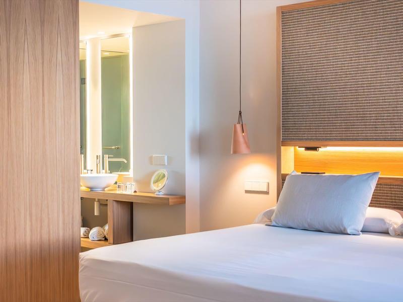 Modernes Schlafzimmer mit großem Bett, hellblauen Kissen, Holzpaneel und indirekter Beleuchtung.