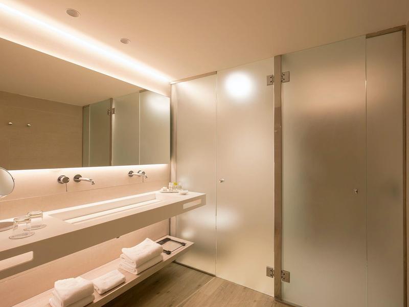 Modernes Badezimmer mit großem Spiegel, beleuchtetem Waschbecken und Glasduschtür in warmem Licht.