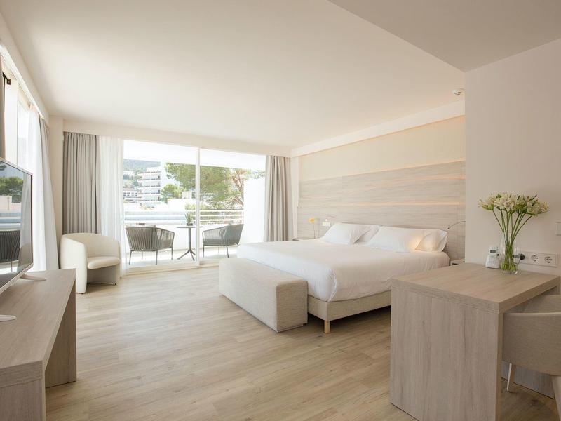 Helles Hotelzimmer mit großem Bett, Holzfußboden, TV, Schreibtisch und Balkon mit Blick ins Freie.