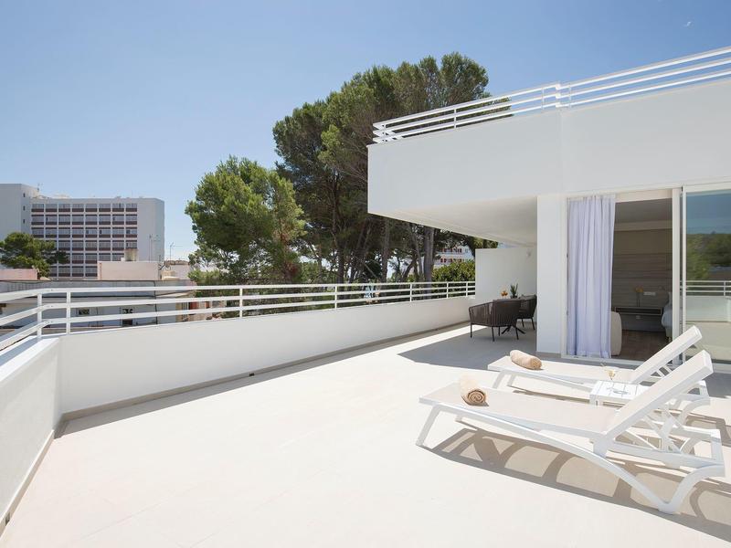 Große weiß geflieste Terrasse mit Sonnenliegen und moderner Balkonbrüstung bei klarem Himmel.