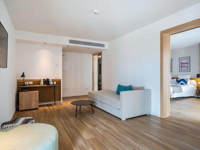 Moderní hotelový obývací pokoj s pohovkou, konferenčním stolkem a výhledem do sousední ložnice.