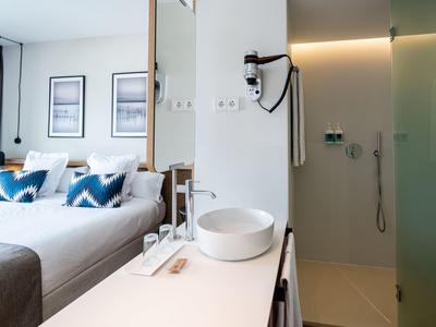 Moderní hotelový pokoj s manželskou postelí a otevřenou koupelnou se sprchou se skleněnými dveřmi.