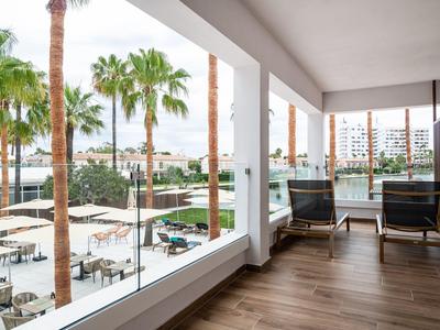 Hotelová terasa s pohodlnými křesly, výhledem na palmy a venkovní bazén.