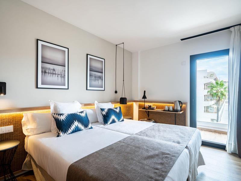 Světý pokoj hotelu s dvojlůžky, moderním zařízením a přístupem na balkon.