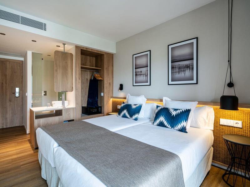 Moderní hotelový pokoj s manželskou postelí, jednoduchým dekorem a jemným osvětlením.