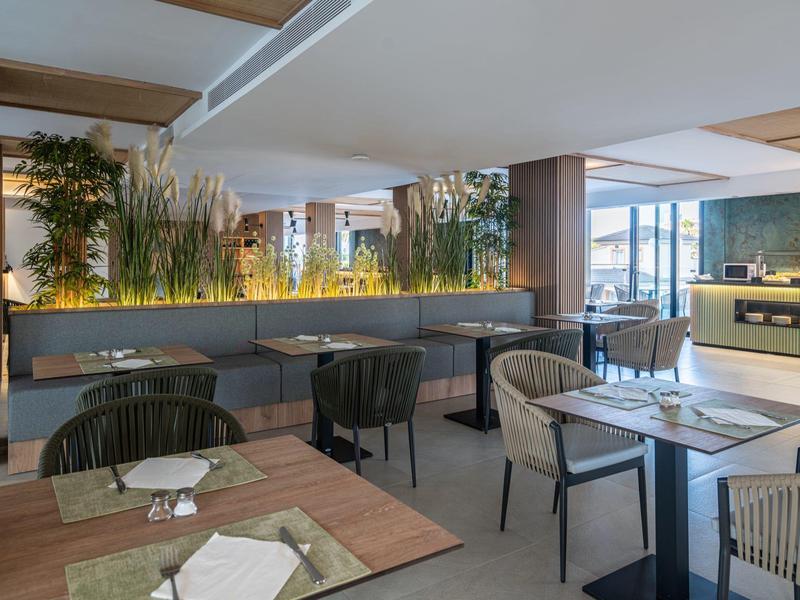 Moderní restaurace s dřevěnými stoly, pohodlnými židlemi a rostlinnou dekorací.