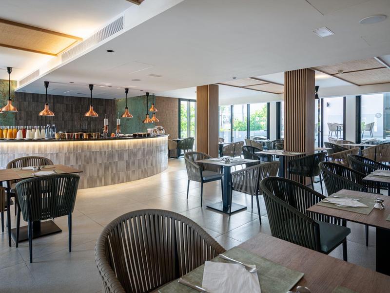 Moderní hotelová jídelna s dřevěnými stoly a velkými okny.