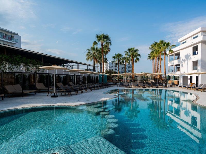 Moderní hotelový bazén s palmami pod jasně modrou oblohou.