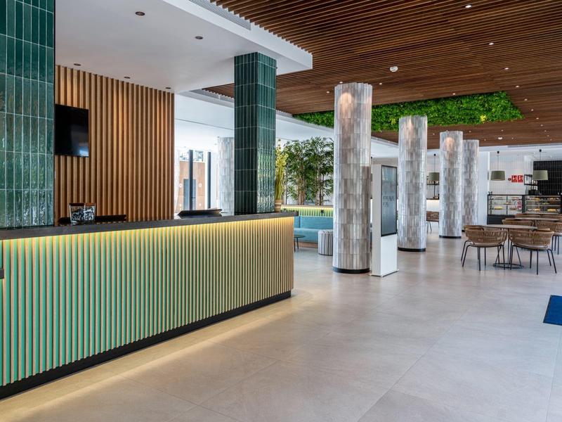 Moderní hotelová recepce se světlým pultem a mramorovými sloupy v prostorném prostoru.