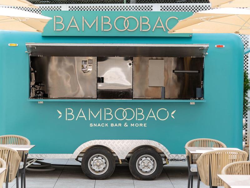 Tyrkysový plážový bar BAMBOOBAO v přívěsu s proutěnými stoly a židlemi.