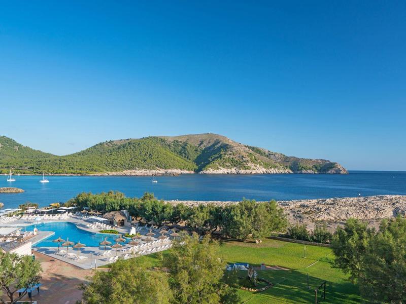Hôtel avec piscine et jardin face à une plage et une mer bleue sous un ciel dégagé.