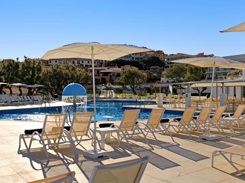 Piscine extérieure avec chaises longues alignées, parasols et collines en arrière-plan.