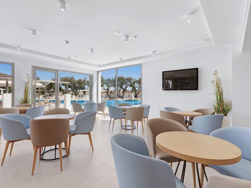 Salle de détente lumineuse avec tables rondes, chaises modernes et grandes fenêtres donnant sur l'extérieur.