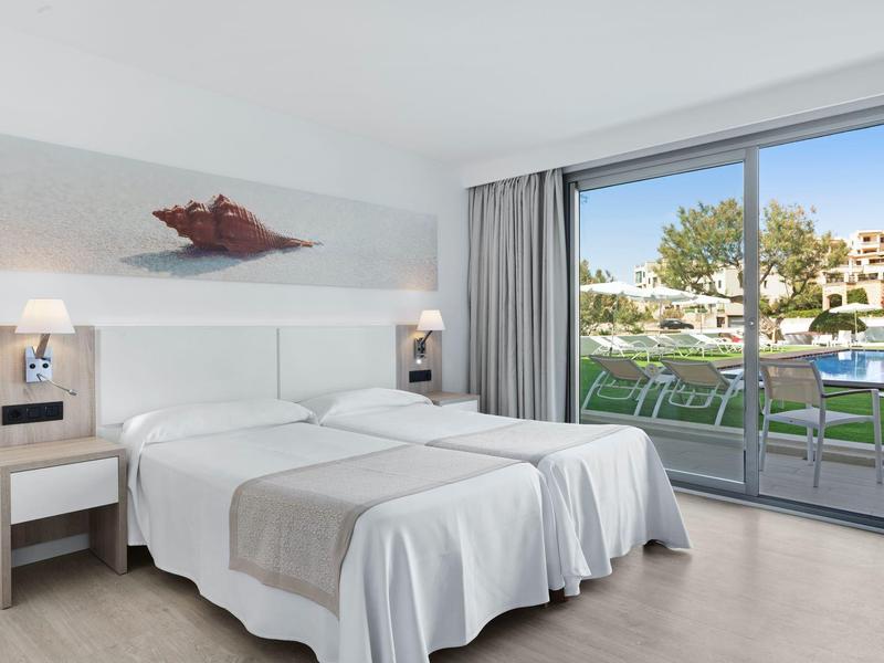 Chambre d'hôtel lumineuse avec lits jumeaux et vue sur une piscine depuis la baie vitrée.