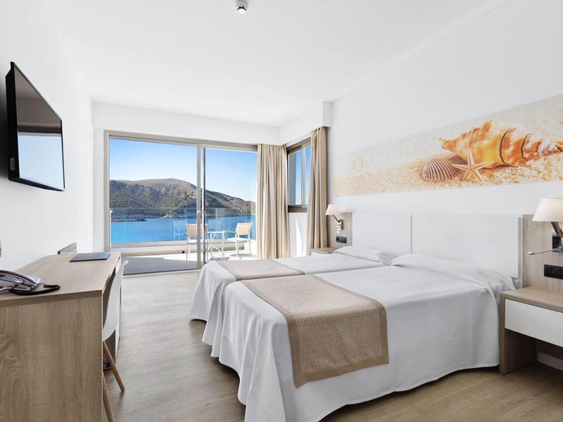 Chambre d'hôtel moderne avec lit double, TV murale et vue sur la mer à travers une baie vitrée.