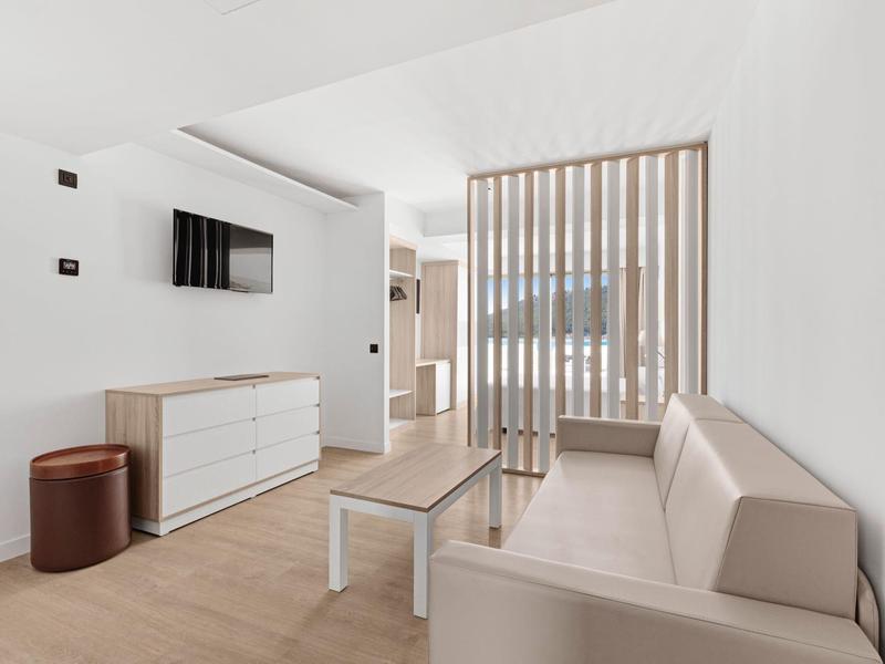 Salon moderne avec canapé beige, table blanche et meuble TV en bois clair.