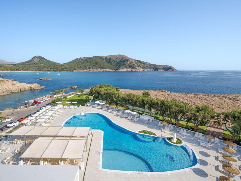Piscine en forme libre avec vue sur la mer et les collines sous un ciel bleu clair.