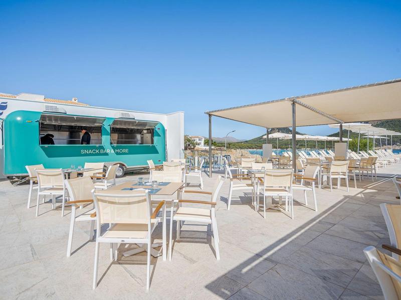 Terrasse extérieure avec tables, chaises et un food truck turquoise sous un ciel bleu clair.