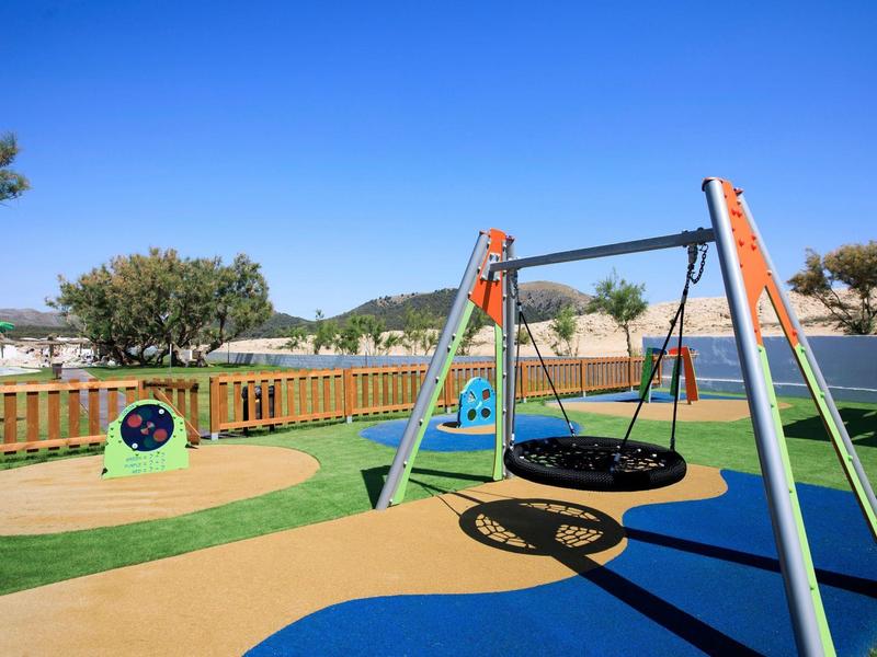 Aire de jeux avec balançoires, sol coloré et ciel bleu clair en arrière-plan.