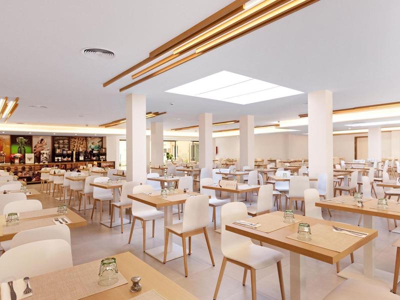 Grande salle de restaurant moderne avec tables en bois et fauteuils beiges.