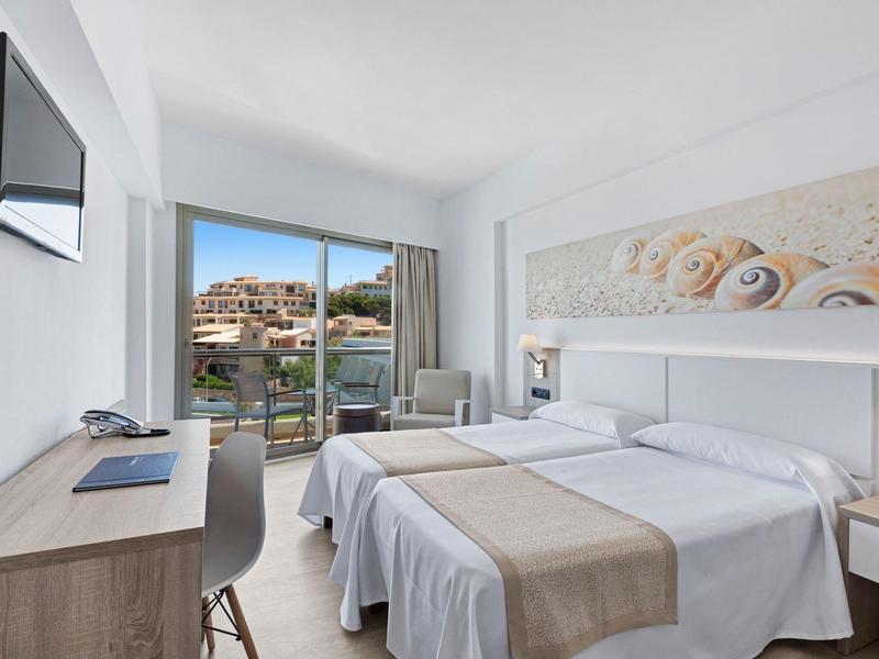 Chambre d'hôtel lumineuse avec lit double, bureau, TV murale et balcon avec vue sur la mer.