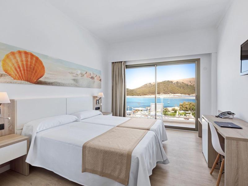 Chambre d'hôtel lumineuse avec lit double, balcon donnant sur une vue sur la mer et la montagne.